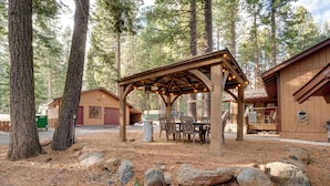 Ein rustikaler Holzpavillon mit Tisch und Stühlen, umgeben von Felsen und Kiefern.