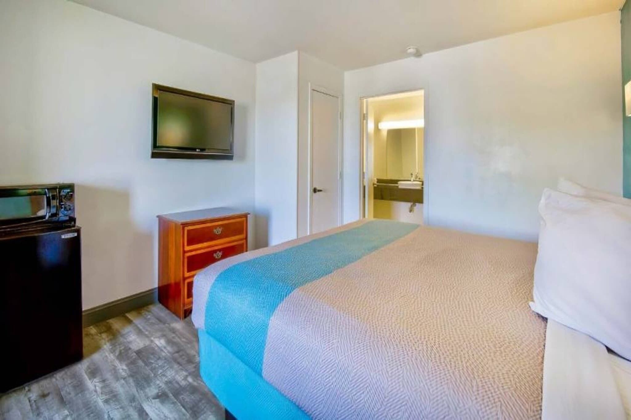 Ett hotellrum med en säng, en tv, en byrå och ett badrum som syns genom en öppen dörr.