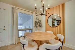 Ein Essbereich mit einem runden Holztisch, sechs Stühlen, einer Pendelleuchte, einem Spiegel und einem Blumentopf.