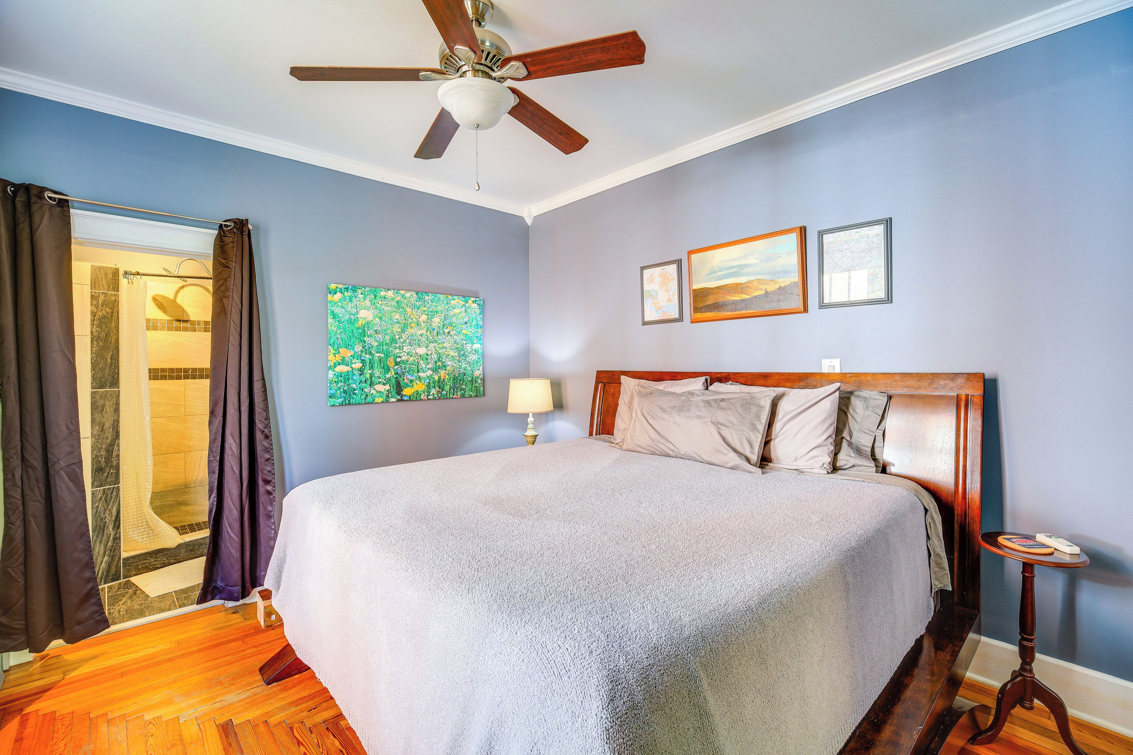 A bedroom with a bed, a ceiling fan, a nightstand, and a shower area.