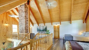 A spacious loft-style room with a wooden ceiling, a brick fireplace, a balcony, and a bed with a blanket. - Mount Rainier Views & Hot Tub: Pet-Friendly Cabin! (Mineral)