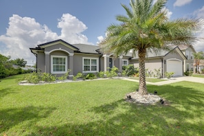 A residential house with a well-maintained lawn, a palm tree, and a garage.