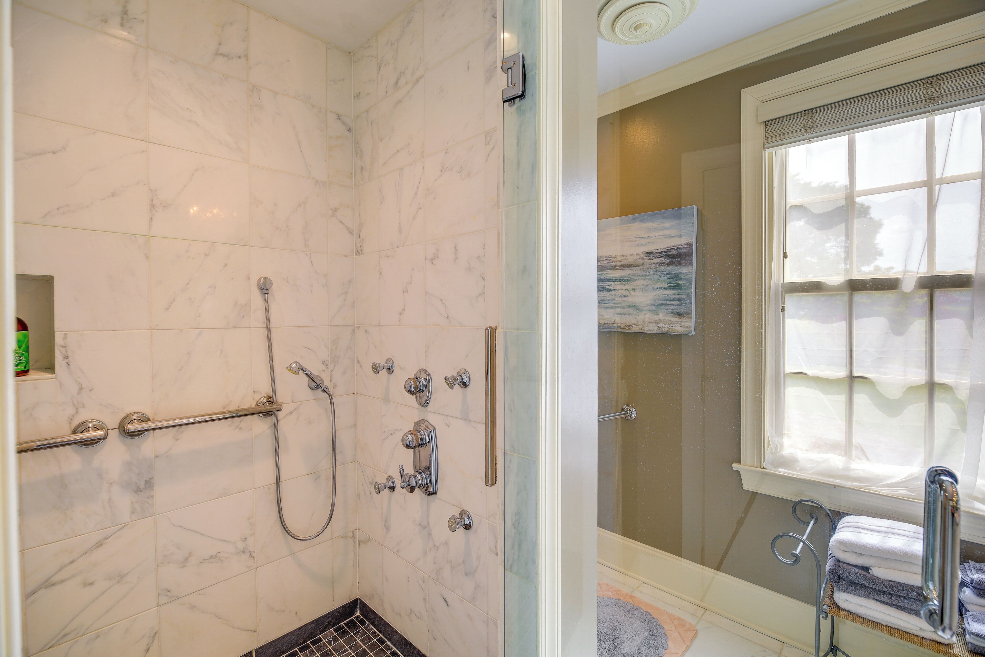 Baño con cabina de ducha de vidrio, barras de apoyo, toallero y ventana con persianas.