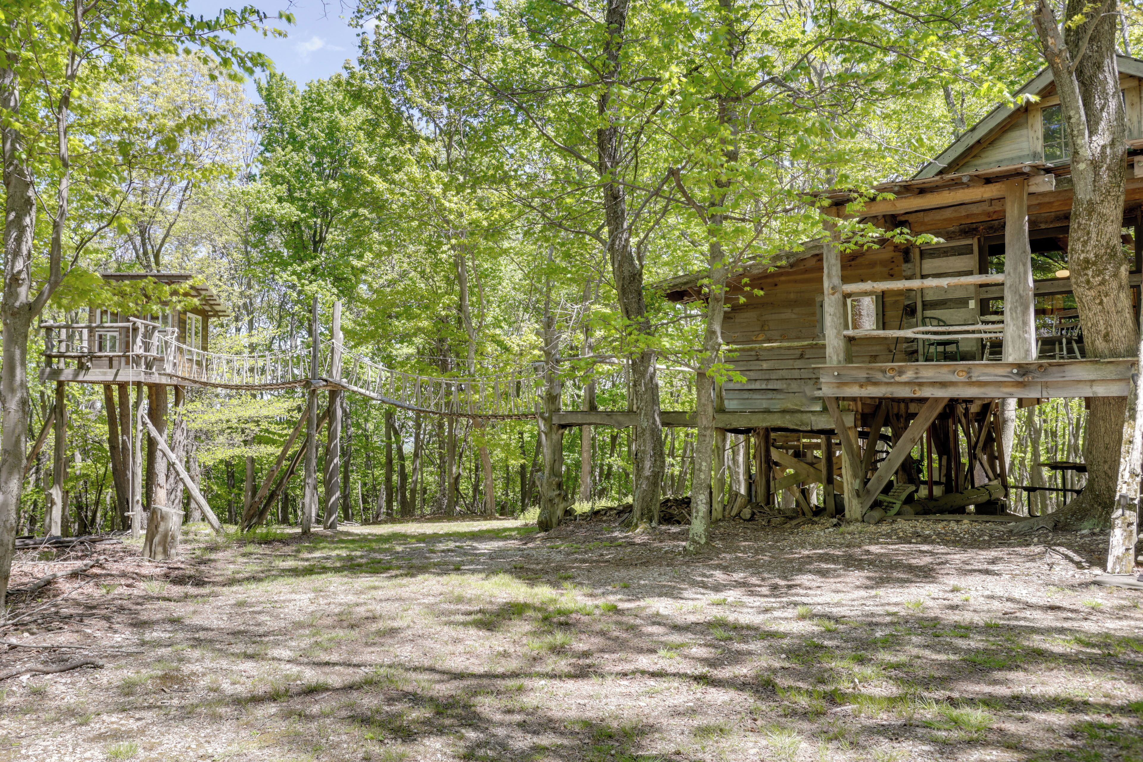 A rustic cabin with a wooden deck and a small porch, surrounded by trees.