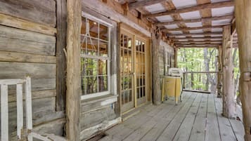 A rustic wooden cabin with a porch, large windows, and a view of the forest.