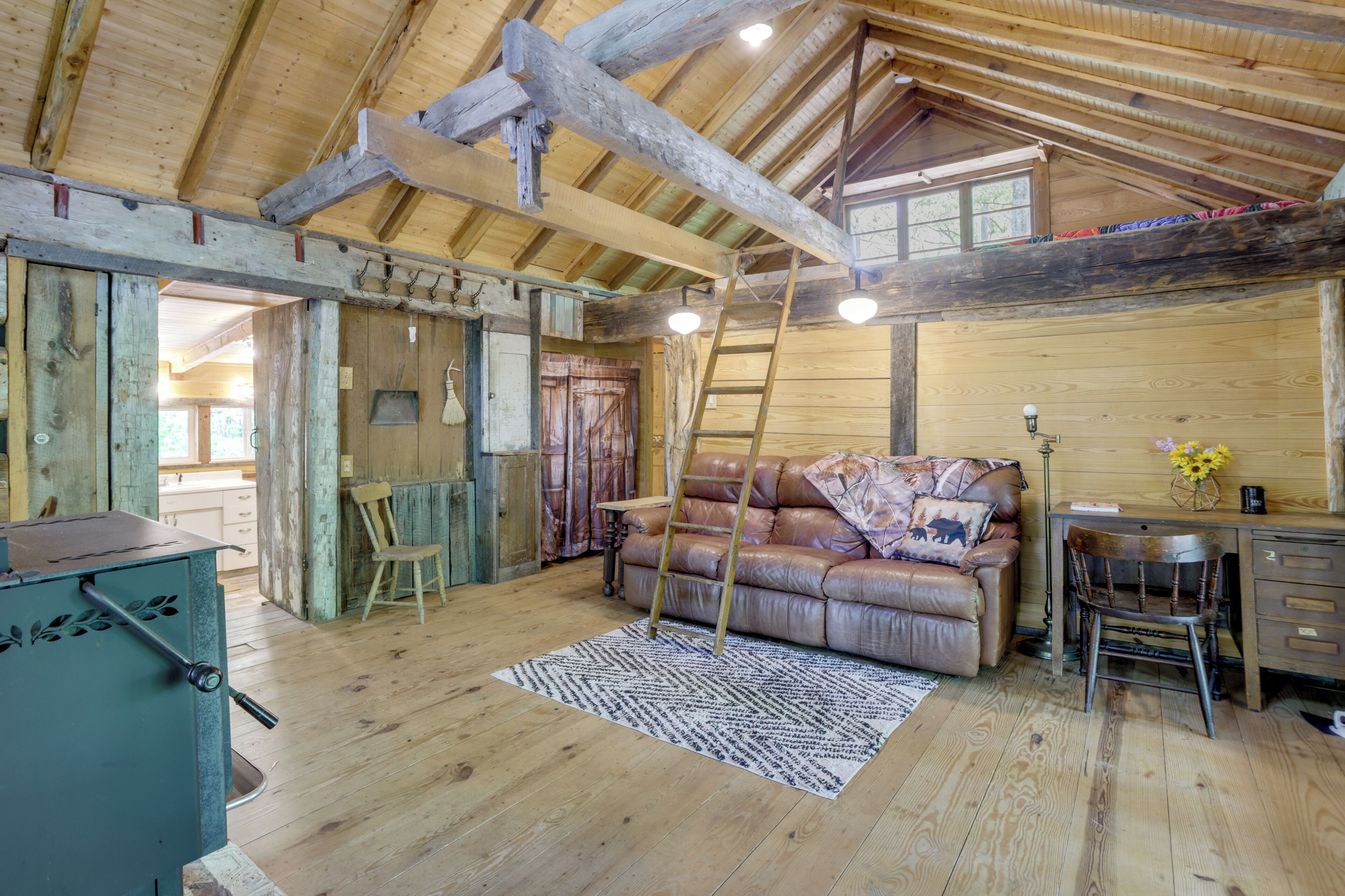 A rustic wooden interior with a lofted ceiling, a leather sofa, a desk, and a ladder.