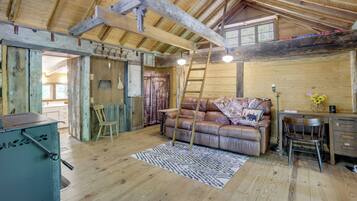 A rustic wooden interior with a lofted ceiling, a leather sofa, a desk, and a ladder.