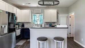 Una cocina moderna con armarios blancos, electrodomésticos de acero inoxidable, una barra con taburetes y una lámpara colgante.