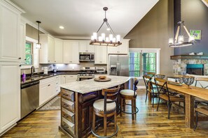 A spacious kitchen with white cabinetry, a large island, and a dining area with wooden chairs and a table.