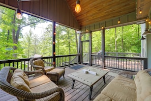 A covered outdoor deck with wicker furniture, a table, and string lights.