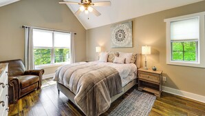Une chambre à coucher comprenant un lit, une chaise, un ventilateur de plafond, une fenêtre et une lampe fixée au mur.