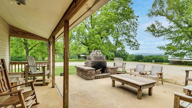 Une terrasse extérieure aménagée avec du mobilier en bois, un foyer en pierre et une vue sur une zone boisée.