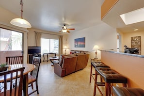 Ein Wohnzimmer mit Sofa, Fernseher, Esstisch, Stühlen und Deckenventilator.