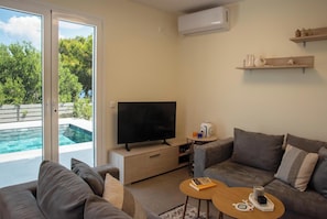 Ein modernes Wohnzimmer mit Flachbildfernseher, grauen Sofas, einem Couchtisch und Blick auf einen Pool.