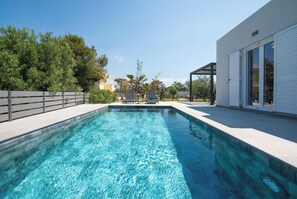 Ein rechteckiger Swimmingpool mit klarem, blauem Wasser, umgeben von einer weißen Liegefläche und einem Holzzaun.
