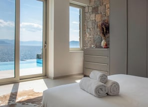 Ein Schlafzimmer mit großem Fenster, Steinwand und Meerblick.