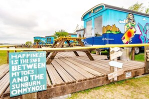 Un autobús azul con un mural, una terraza de madera y un letrero con una cita.