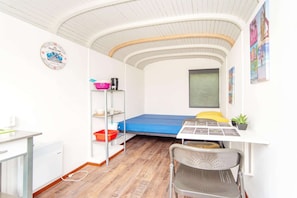 Une petite pièce comprenant un lit superposé, un bureau avec une chaise, une petite étagère, une horloge et une fenêtre.