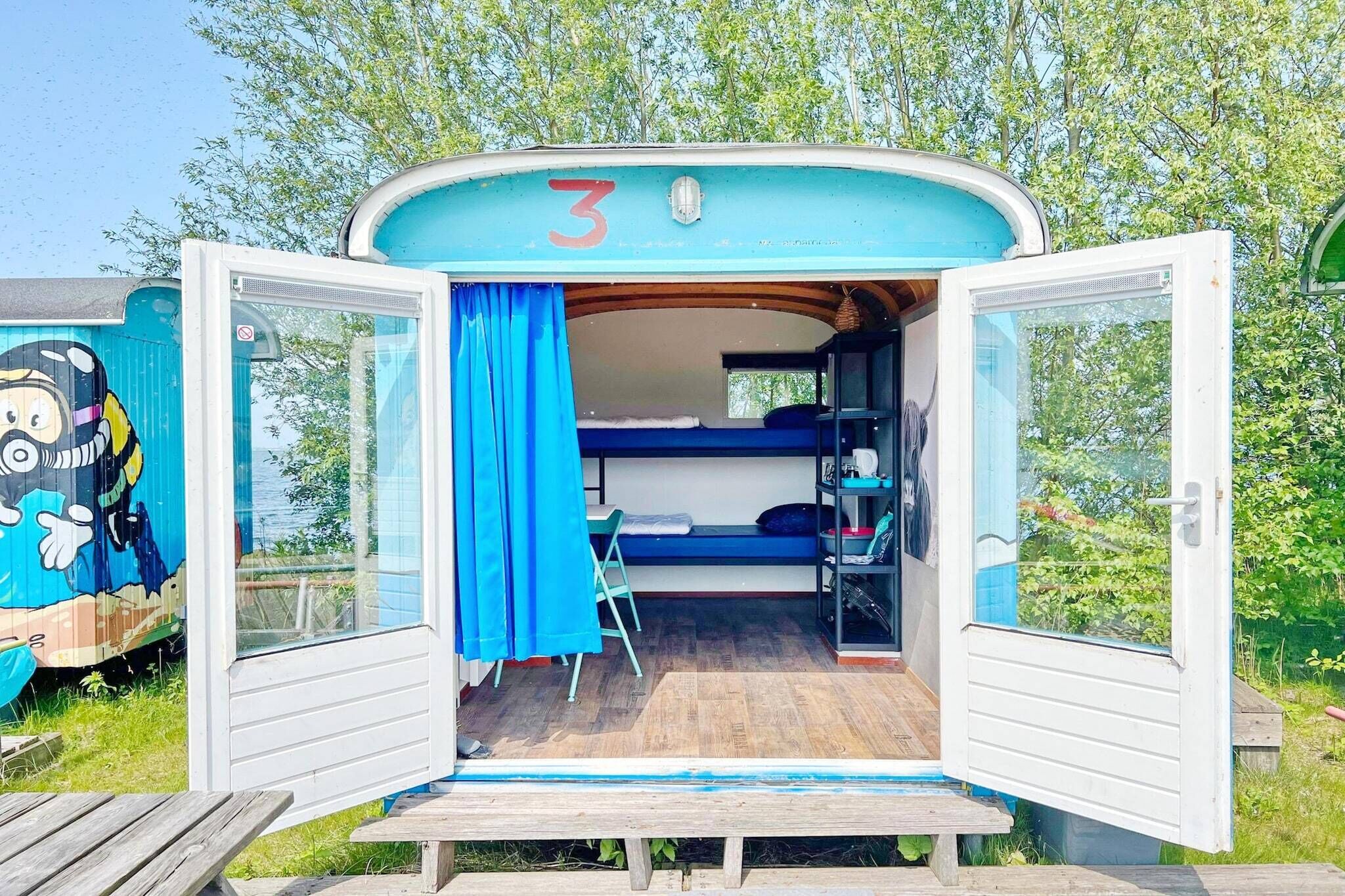 A small, open RV with a number 3 on the front, a bunk bed inside, and a table outside.