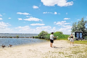Een strand met een heldere lucht, een waterpartij en een klein gebouw op de achtergrond.