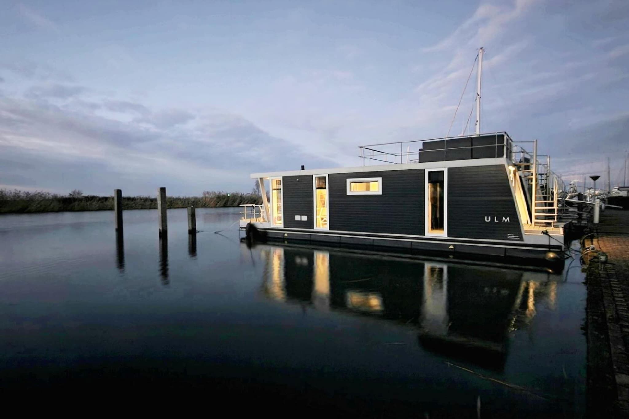 Een moderne, smalle boot aangemeerd aan een kalm waterlichaam, met een heldere lucht.
