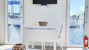 A room with a white table, a television mounted on the wall, and a view of boats through large windows. - Floating lodge with Terrace in Lelystad (Lelystad)