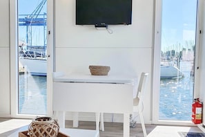 Une pièce avec une table blanche, un téléviseur fixé au mur et une vue sur les bateaux à travers de grandes fenêtres.