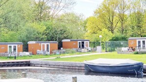 A row of mobile homes by a canal with a dock and picnic area. - Cozy Tiny Wagon by the Marina (Naarden)