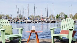 A dock with two green Adirondack chairs, a small round table, and a view of a marina with numerous boats. - Cozy Tiny Wagon by the Marina (Naarden)