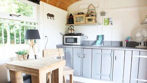 A kitchen with a wooden table and chairs, a microwave, a kettle, and cabinets. - Cozy Tiny Wagon by the Marina (Naarden)