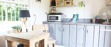 Une cuisine avec une table et des chaises en bois, un four à micro-ondes, une bouilloire et des placards.