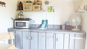 A kitchen with a microwave, kettle, and coffee maker on the counter, a fan, and wooden cabinets. - Cozy Tiny Wagon by the Marina (Naarden)