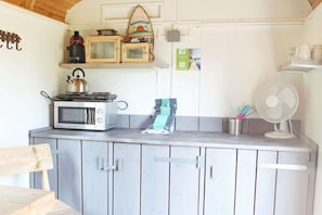 Une cuisine équipée d’un four à micro-ondes, d’une bouilloire et d’une machine à café sur le plan de travail, d’un ventilateur et de placards en bois.