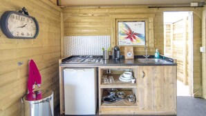 Una cocina compacta con un reloj, un refrigerador, un lavamanos y un cuadro decorativo de una mariposa.