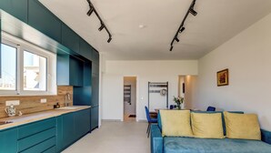 Une cuisine moderne avec des meubles de couleur turquoise, un plan de travail en bois et un coin repas agrémenté d’un canapé bleu et de coussins jaunes.