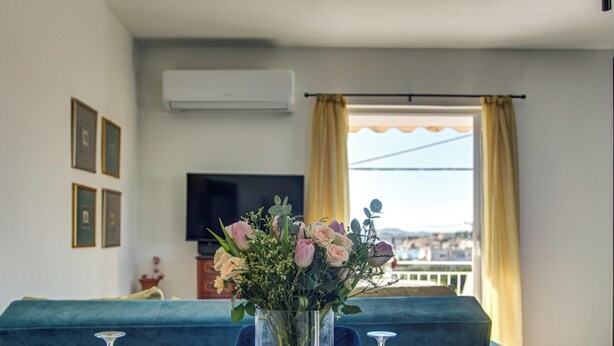 Un salon avec un canapé, un téléviseur, une fenêtre avec des rideaux et un vase rempli de fleurs.