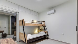 Une chambre avec un lit superposé, un bureau et une chaise, une porte-fenêtre coulissante et un appareil de climatisation.