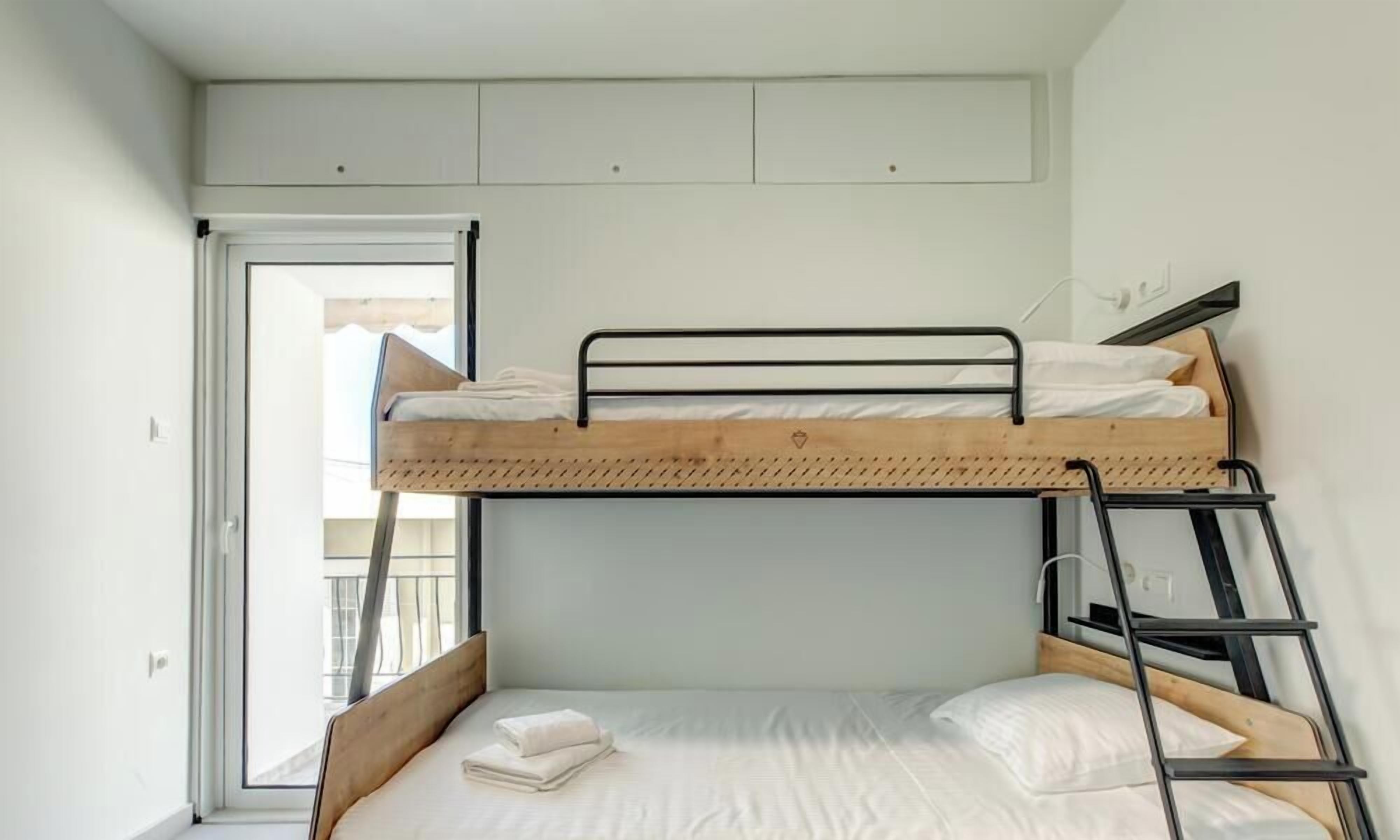 Une chambre avec un lit superposé, une fenêtre, une échelle et une petite étagère en bois au-dessus du lit.