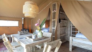 A tented room with a wooden table, chairs, a hanging light fixture, and a bed with a canopy. - Luxury Safari Lodge Escape for 5 (Almere)