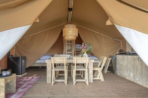 Eine Zelthütte mit Bett, Holztisch, Stühlen, einer Pendelleuchte und einer kleinen Küchenzeile.
