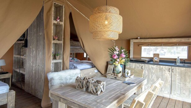 A cozy tented accommodation with a wooden table, chairs, a hanging light fixture, and a window with a view. - Luxury Safari Lodge Escape for 5 (Almere)