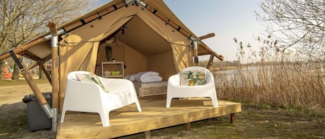 A tent with two white chairs, a bed, and a small table.