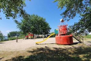 Un parque infantil con tobogán, estructura para escalar y un pequeño edificio.