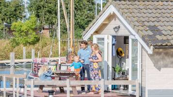 A family at a dock with a small house, a boat, and a table with chairs.