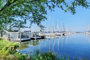 A marina with multiple sailboats docked, a glass building, and calm water.