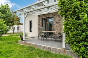 A modern house with a patio, a table, and chairs. - Apartment 'Für 2 Personen 35 M²' with Private Terrace, Private Garden and Wi-Fi (Koserow)