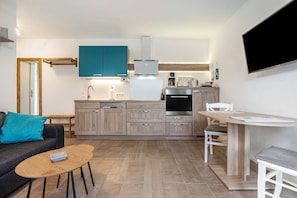 A modern kitchen with a dining area, a sofa, and a TV mounted on the wall. - Apartment 'Für 2 Personen 35 M²' with Private Terrace, Private Garden and Wi-Fi (Koserow)