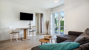 Ein modernes Wohnzimmer mit Flachbildfernseher, einem Esstisch, zwei Stühlen, einer Couch und einem kleinen Couchtisch.