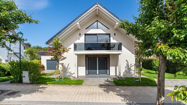 Ein modernes, zweistöckiges Haus mit Balkon, Garage und gepflegtem Garten.