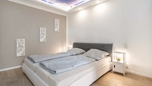 Ein modernes Schlafzimmer mit Bett, Nachttischen, Wandkunst und einer Dachfensterdecke.